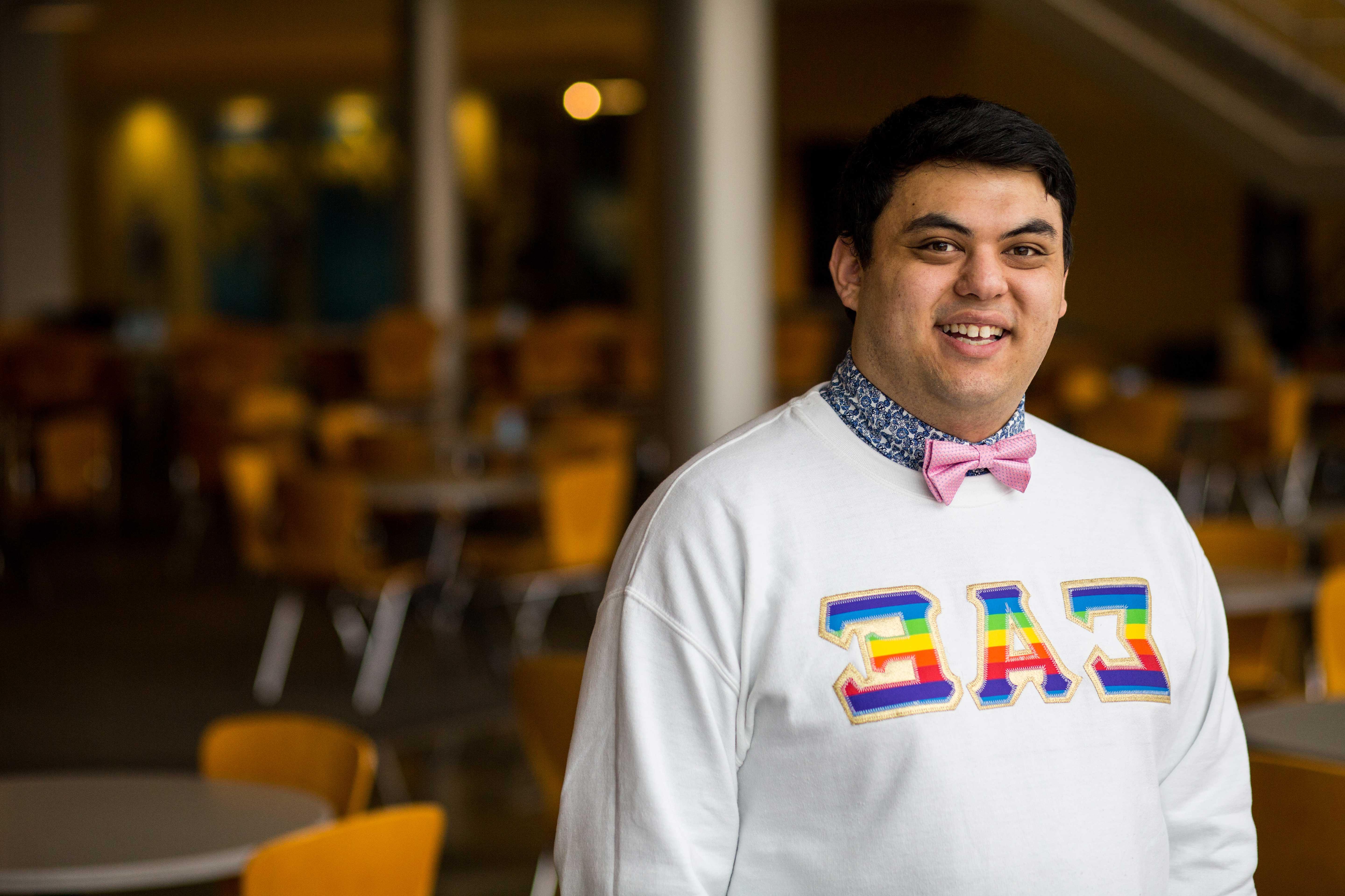 一名UMKC学生(以拉丁裔男性的身份出现)穿着印有彩虹色希腊字母的运动衫自豪地站着.
